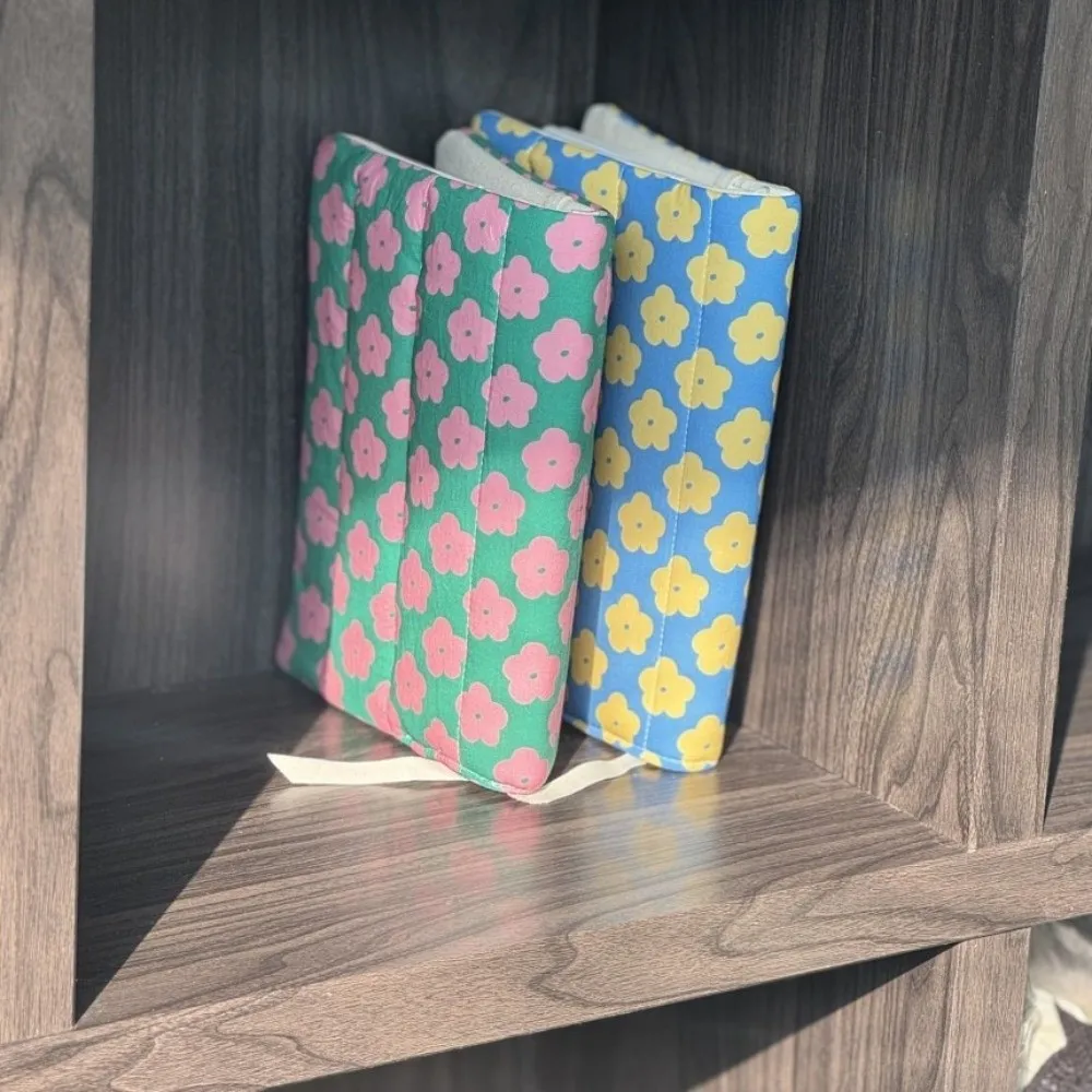 Deux couvre-livres matelassés à grosses fleurs, vert et bleu, debout sur une étagère